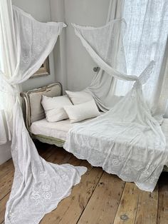 a white bed sitting in a bedroom next to a window with curtains on top of it