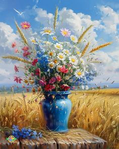 a blue vase filled with lots of flowers on top of a wooden table next to a field