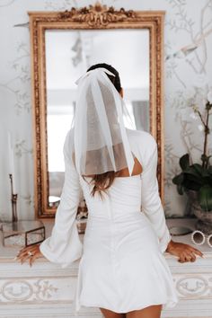 the back of a woman's head wearing a veil and white dress in front of a mirror