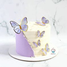 a white cake with purple frosting and butterflies on top, sitting on a plate