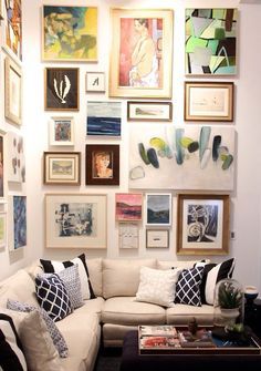 a living room filled with lots of framed pictures on the wall above a white couch