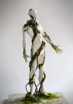 a white statue with green vines on it's body and hands, standing in front of a gray background