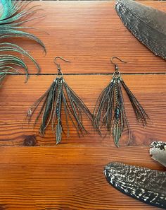 three pairs of feather earrings sitting on top of a wooden table next to two feathers