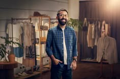 a man standing in front of a clothing rack with his hands in his pockets and looking at the camera