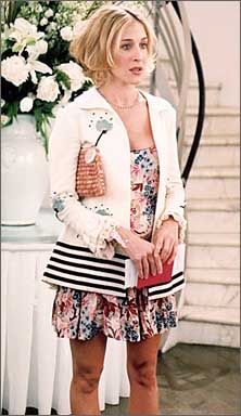 a woman standing in front of a vase with flowers on the wall behind her and holding a purse