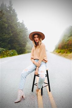 a woman sitting on top of a chair in the middle of an empty road with trees behind her