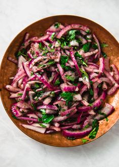 a wooden bowl filled with chopped red onions and greens on top of a white table