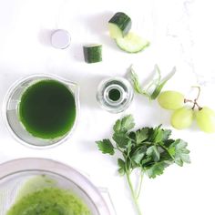 a blender filled with green liquid next to some fruits and vegetables on a white surface