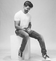 a young man sitting on top of a white cube with his hands in his pockets