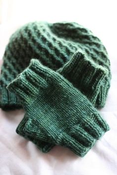 two green knitted mittens laying on top of a bed