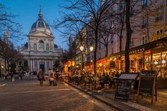 people are sitting at tables on the sidewalk in front of a building with a dome