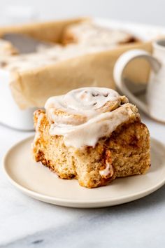 a cinnamon roll sitting on top of a white plate next to a cup of coffee