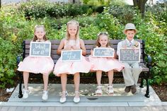 three children sitting on a bench holding signs