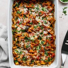 a casserole dish with meat and vegetables in it on a white table next to silverware