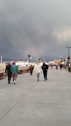 people walking on the boardwalk with a rainbow in the sky behind them and dark clouds overhead