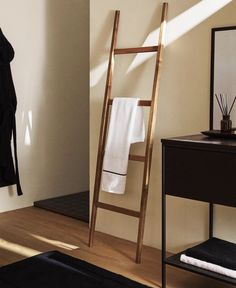 a wooden ladder leaning against a wall next to a mirror and towel rack with towels on it