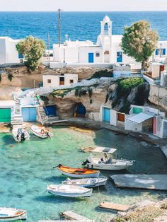 several small boats are docked in the clear blue water next to white buildings and cliffs