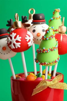 christmas cake pops in a red cup with snowmen and trees on them, all decorated to look like santa's helpers