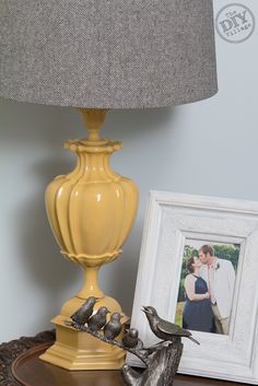 two birds sitting on a table next to a lamp with a picture in front of it