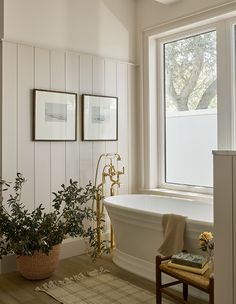 a bathroom with a tub and two plants in the corner, along with pictures on the wall