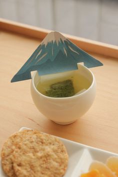 a bowl of soup and crackers on a table with a paper cut out of a mountain