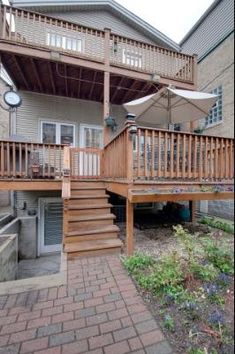 a deck with an umbrella and steps leading up to the back of a house on a brick patio