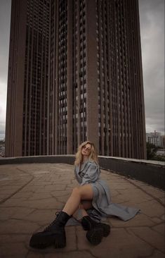 a woman is sitting on the ground in front of a tall building with her legs crossed