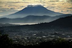 a view of a city with a mountain in the back ground and clouds over it