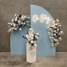 a tall white vase filled with flowers next to a neon sign that says oh baby