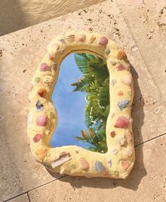 a mirror that is on the ground with shells around it and palm trees in the background