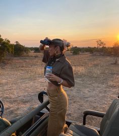 a woman standing in the back of a truck holding a water bottle and looking into the distance