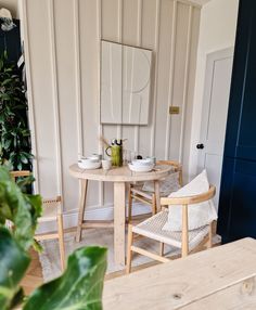 two chairs and a table in a room with white paneled walls, potted plants on either side