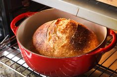 a loaf of bread in a red pot on an oven rack with the door open