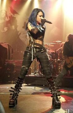 a woman with blue hair and leather pants on stage holding a microphone in her hand