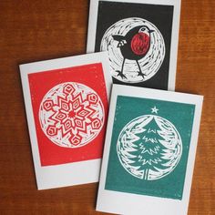 three christmas cards with designs on them sitting on top of a wooden table next to each other