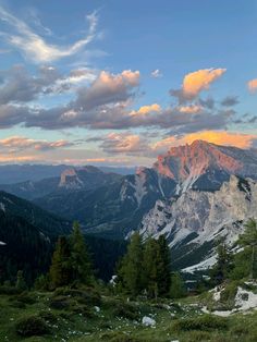 the mountains are covered in snow and green grass as the sun is setting over them