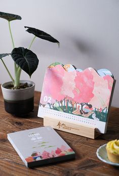 a wooden table topped with a cupcake next to a potted plant and calendar