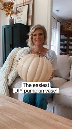 a woman sitting on a couch holding a large pumpkin in front of her face with the caption, the easyest diy pumpkin vase