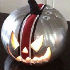 a metal pumpkin with glowing eyes and red ribbon on it's head, sitting on a table