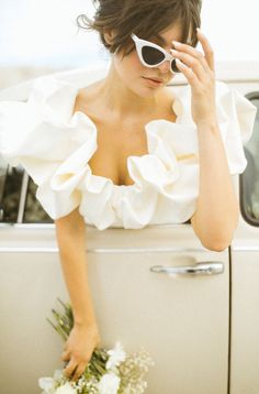 a woman in white dress leaning on the door of a car with sunglasses on her head