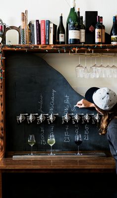 a woman standing in front of a blackboard with wine glasses on top of it