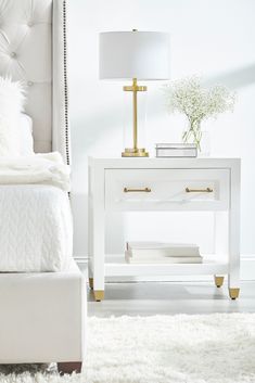 a white bed sitting next to a night stand with a lamp on top of it