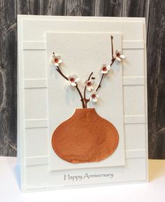 a handmade card with an orange vase and white flowers on the front, against a wooden background