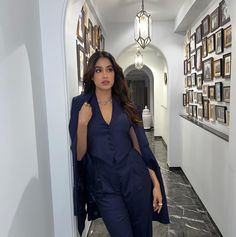 a woman in a blue suit is walking down a hallway with pictures on the wall