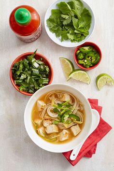 bowls of soup and vegetables on a white table with limes, cilantro