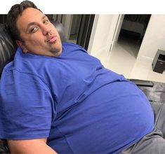 a man laying on top of a black leather couch next to a tv remote control