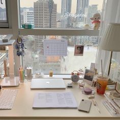 a desk with a laptop computer and various office supplies on it in front of a large window