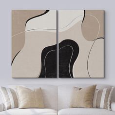 two abstract paintings on the wall in a living room with white couches and pillows