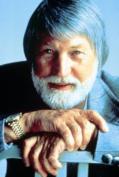 an older man with grey hair and beard sitting on a chair looking at the camera