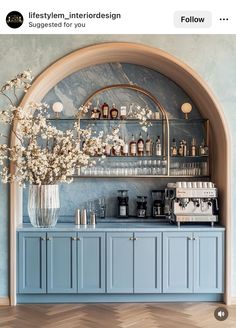 a blue bar with shelves and vases filled with flowers on the counter, in front of an arched window